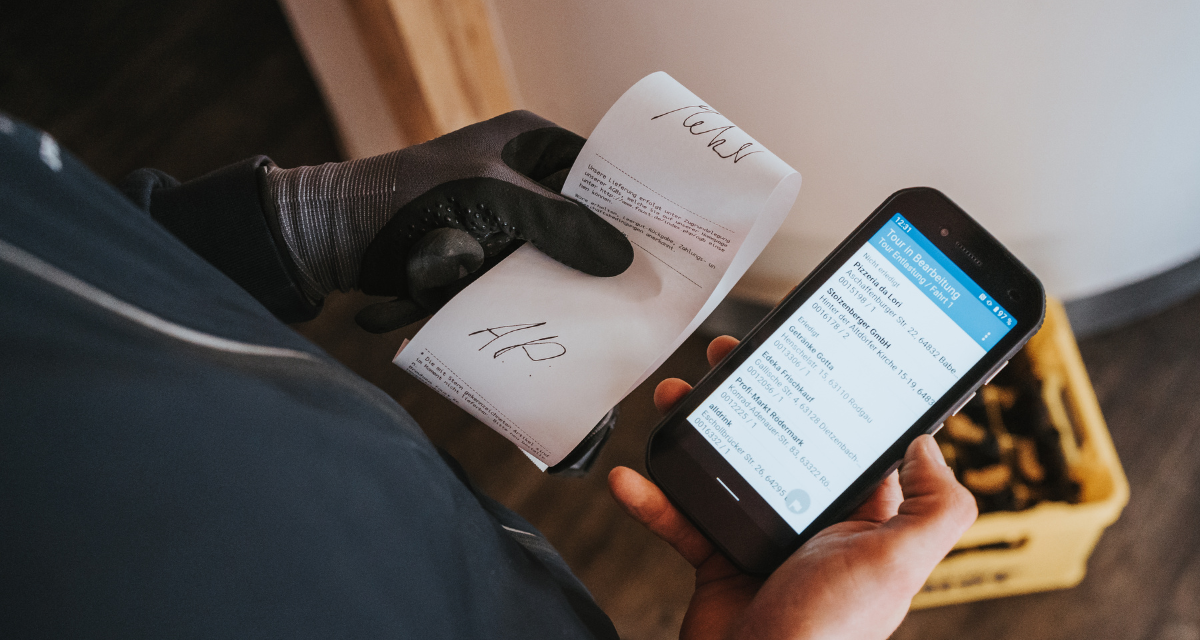 Ein%20Mann%20sitzt%20in%20einem%20Fahrzeug%20und%20bedient%20einen%20mobilen%20Drucker%2C%20w%E4hrend%20er%20einen%20frisch%20gedruckten%20Beleg%20entgegenzieht.%20Eine%20weitere%20Person%20steht%20daneben%20und%20h%E4lt%20das%20Papier%20fest.