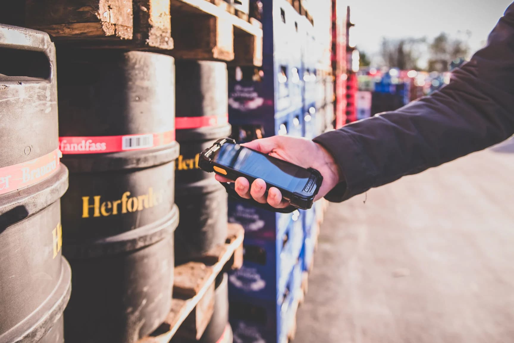 Person%20h%E4lt%20einen%20blauen%20mobilen%20Barcodescanner%20vor%20Gasflaschen%20in%20einem%20Au%DFenlager%2C%20mit%20Herford-Markenflaschen%20im%20Vordergrund