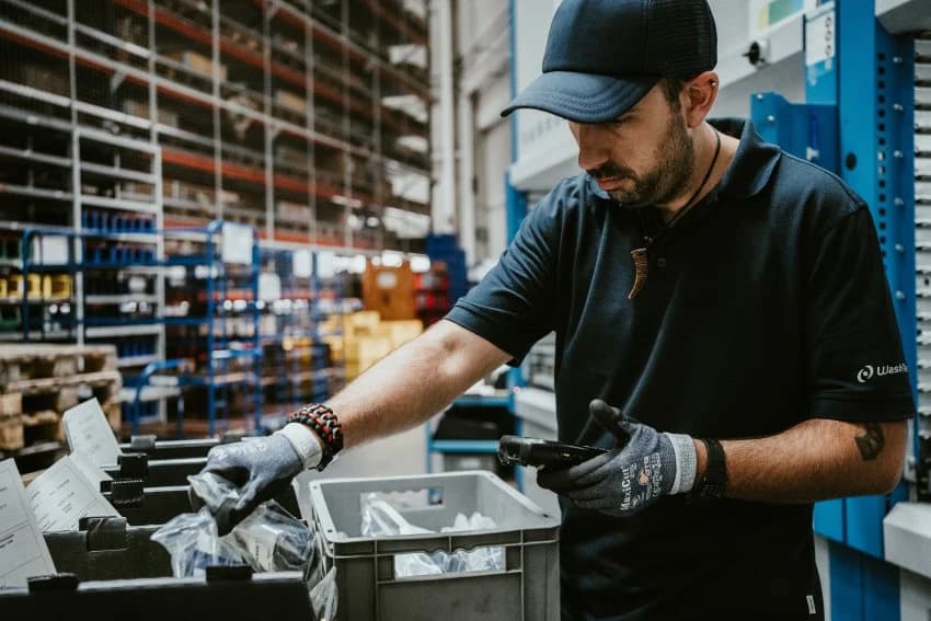 Ein%20Lagermitarbeiter%20bei%20WashTec%20kommissioniert%20Artikel%20aus%20RFID-Beh%E4ltern%20mit%20einem%20mobilen%20Scanner%20vor%20einem%20automatischen%20Kardex%20Shuttle%20Lagerlift.%20Dies%20veranschaulicht%20die%20Integration%20von%20SAP-Logistik%2C%20mobiler%20Datenerfassung%20und%20Smart%20Storage%20f%FCr%20schnellere%2C%20papierlose%20Prozesse.