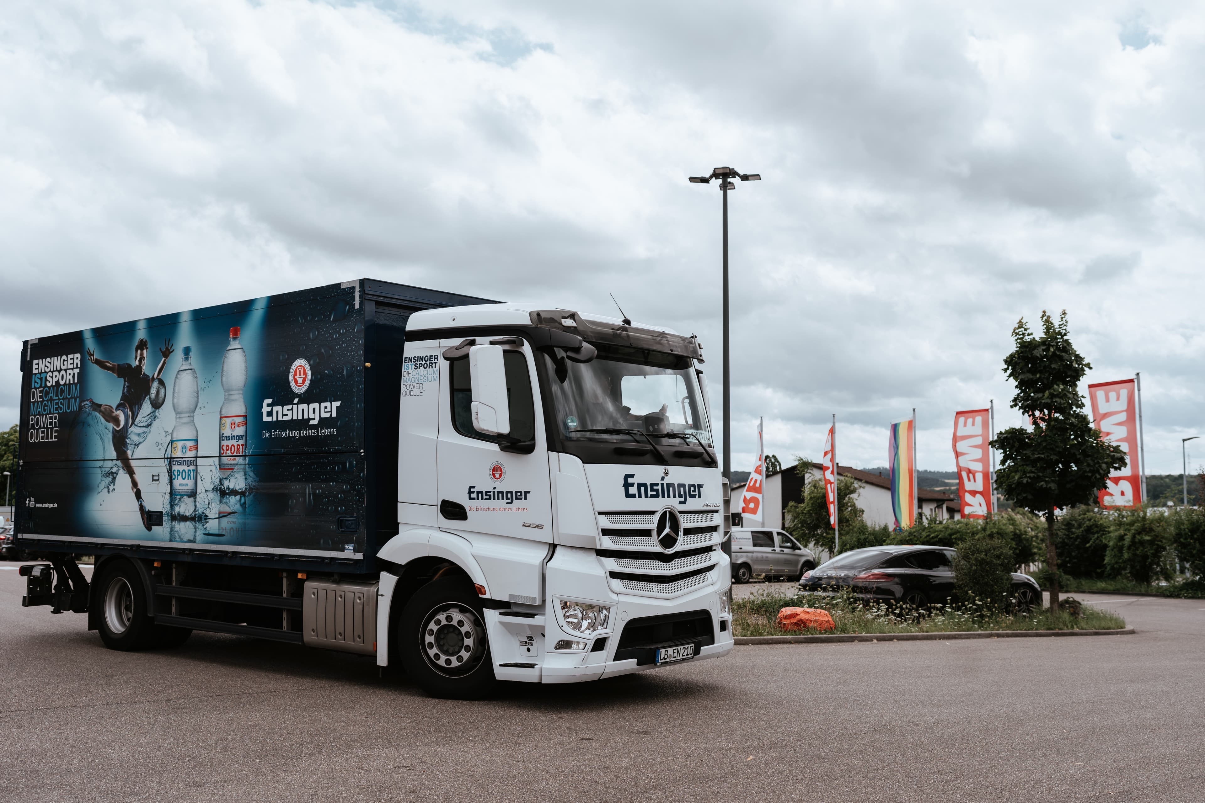 Ensinger%20Lkw%20f%FCr%20Getr%E4nkelogistik%20im%20Au%DFenbereich%20mit%20Werbegrafiken%20auf%20dem%20Auflieger%2C%20die%20Flaschenprodukte%20zeigen%20und%20den%20Getr%E4nketransport%20darstellen.